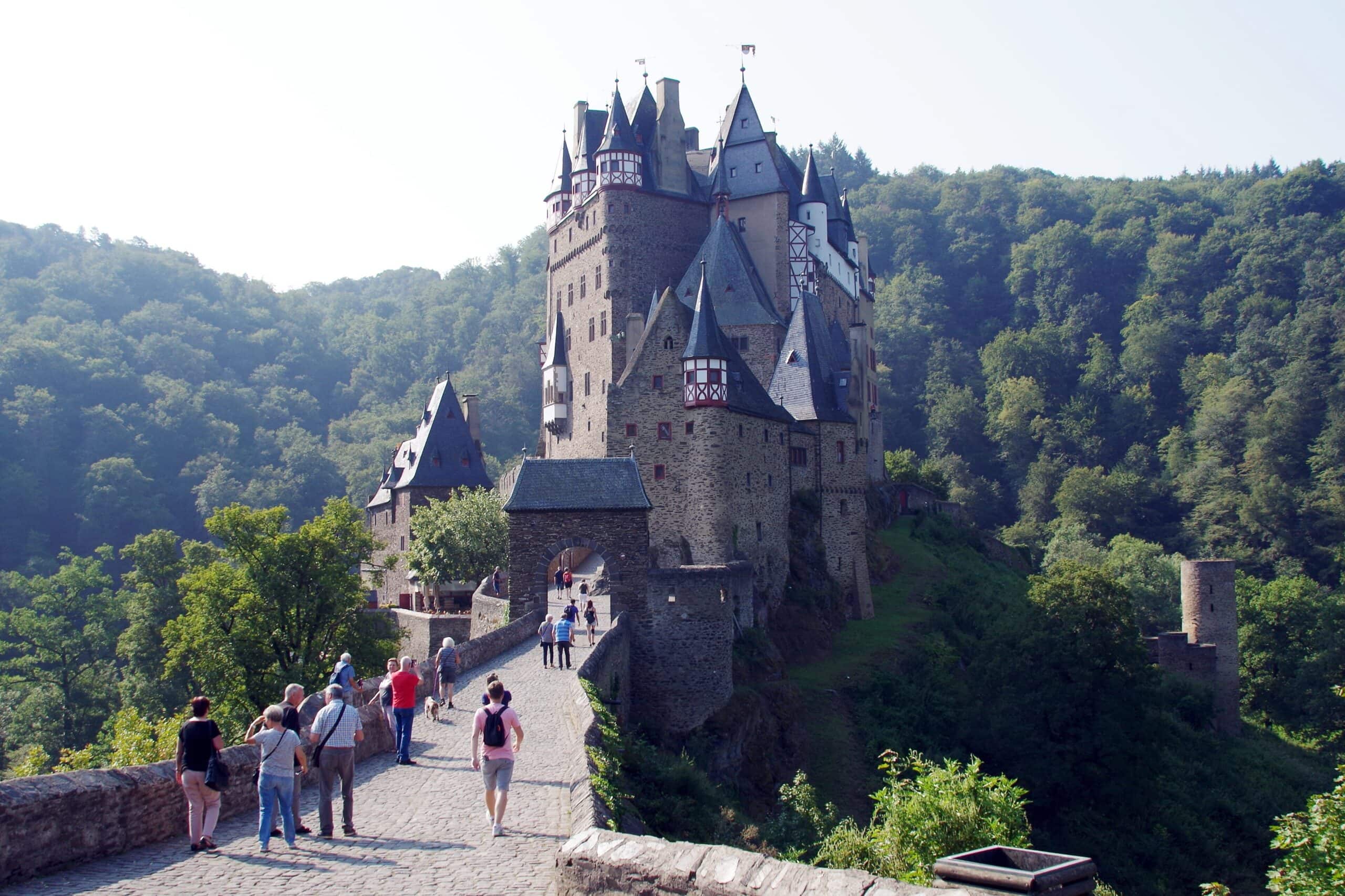 Eltz Castle 6 Visitors walking along the cobblestone bridge approach to the upper courtyard gate of Burg Eltz, with the multi-towered residential cluster rising directly ahead and forested valley walls on either side