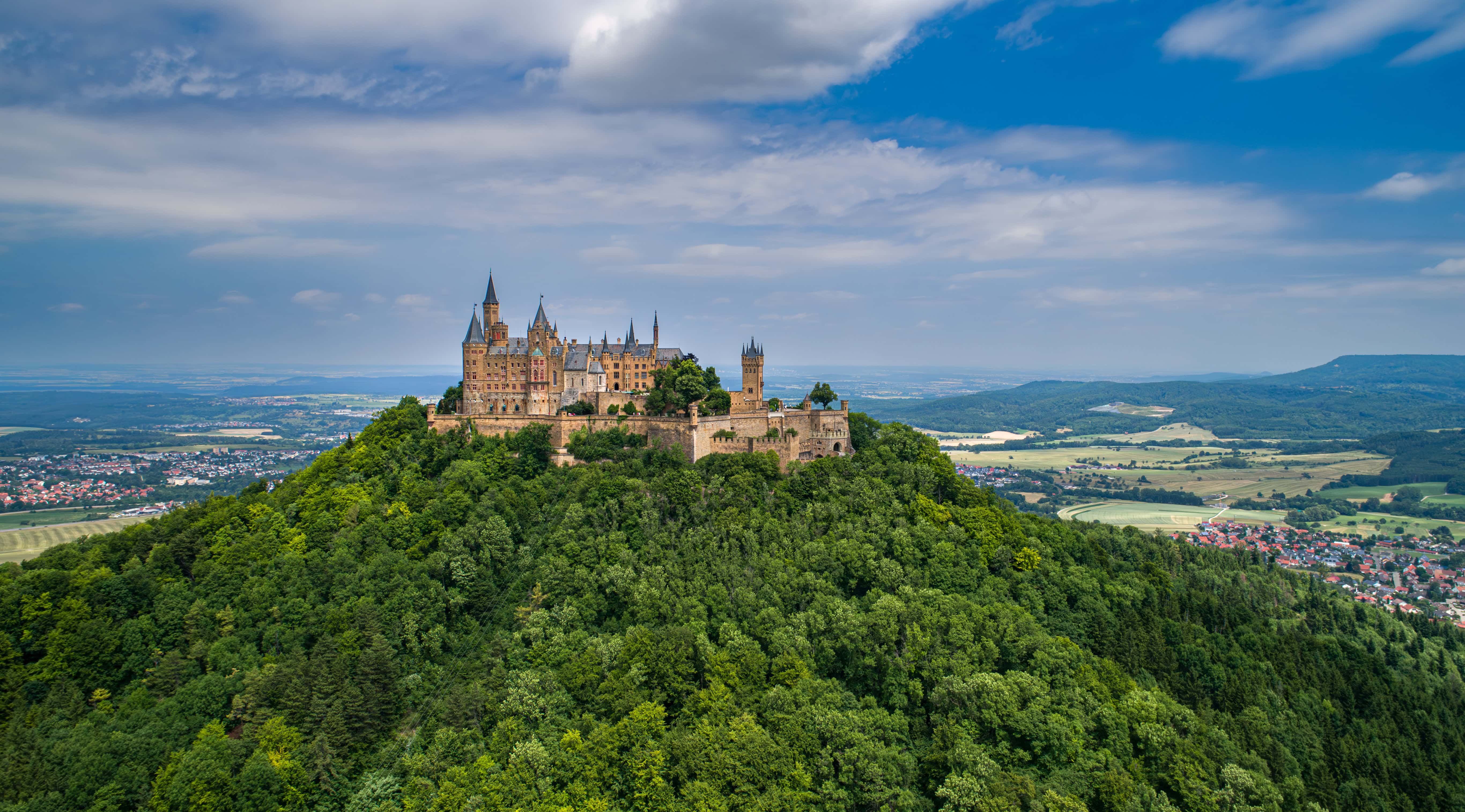 Hohenzollern Castle 3 Hohenzollern Castle seen from a nearby ridge showing the Neo-Gothic towers rising above the wooded summit with dramatic clouds, Baden-Württemberg, Germany