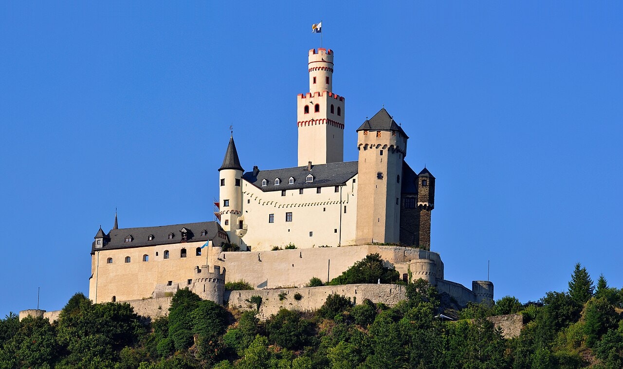 Marksburg Castle on its wooded hilltop, with the tall white keep and its round crenellated cap, the residential range below it, and outer walls stepping down the slope. Marksburg Castle on its wooded hilltop, with the tall white keep and its round crenellated cap, the residential range below it, and outer walls stepping down the slope.