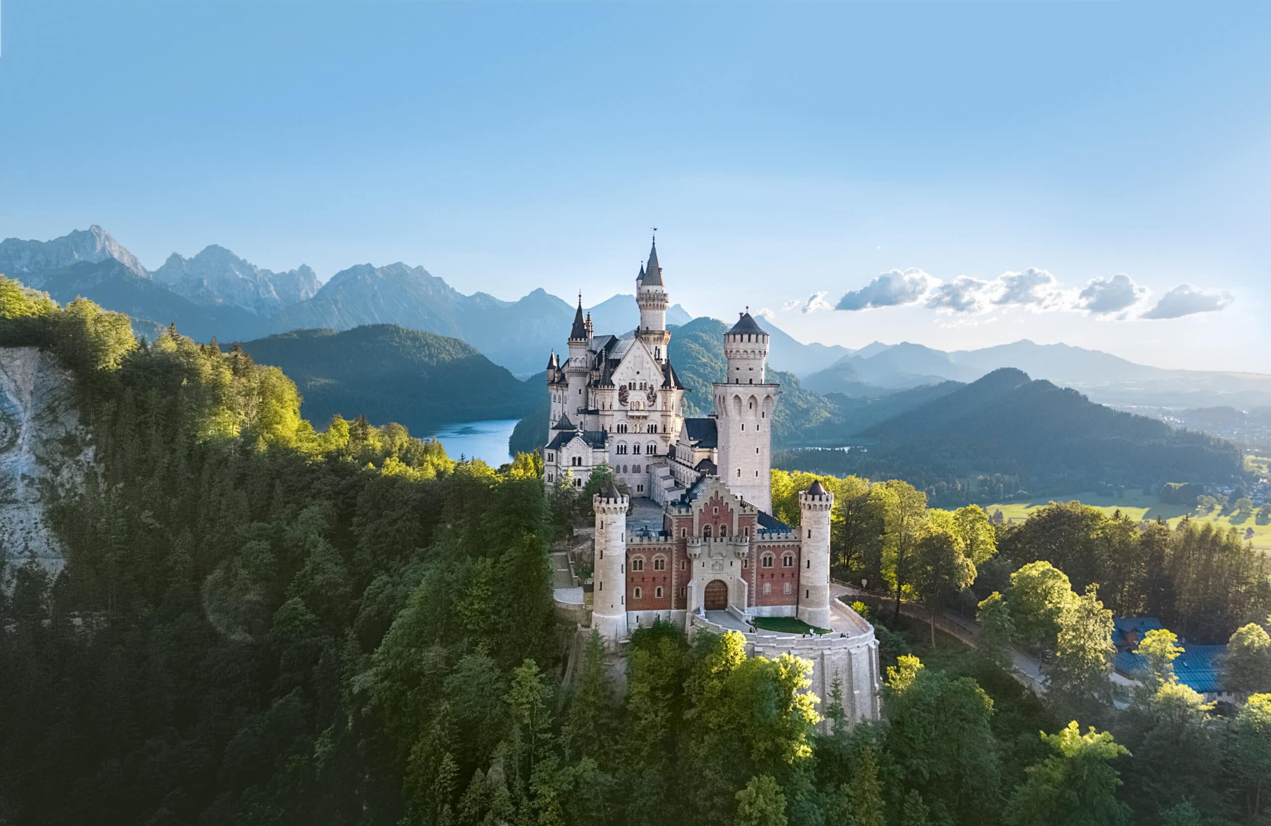 Aerial view of the whole Neuschwanstein complex from the east, with the red-brick Gateway Building in the foreground and the Alps behind Aerial view of the whole Neuschwanstein complex from the east, with the red-brick Gateway Building in the foreground and the Alps behind