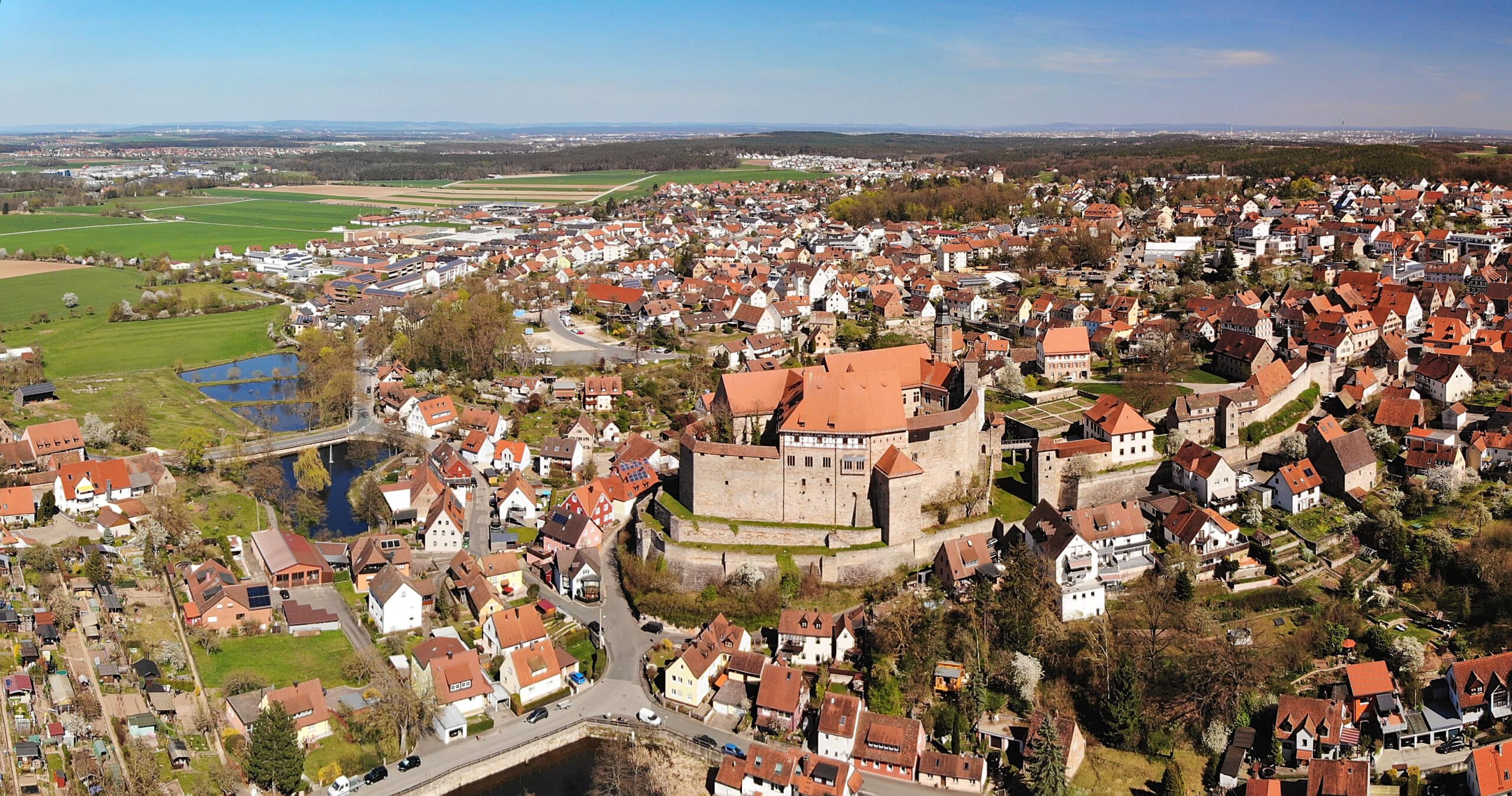 Cadolzburg Castle 8 Aerial photograph of Cadolzburg with castle complex at centre, surrounding village, fields, and pond, with Mittelfranken landscape extending to horizon