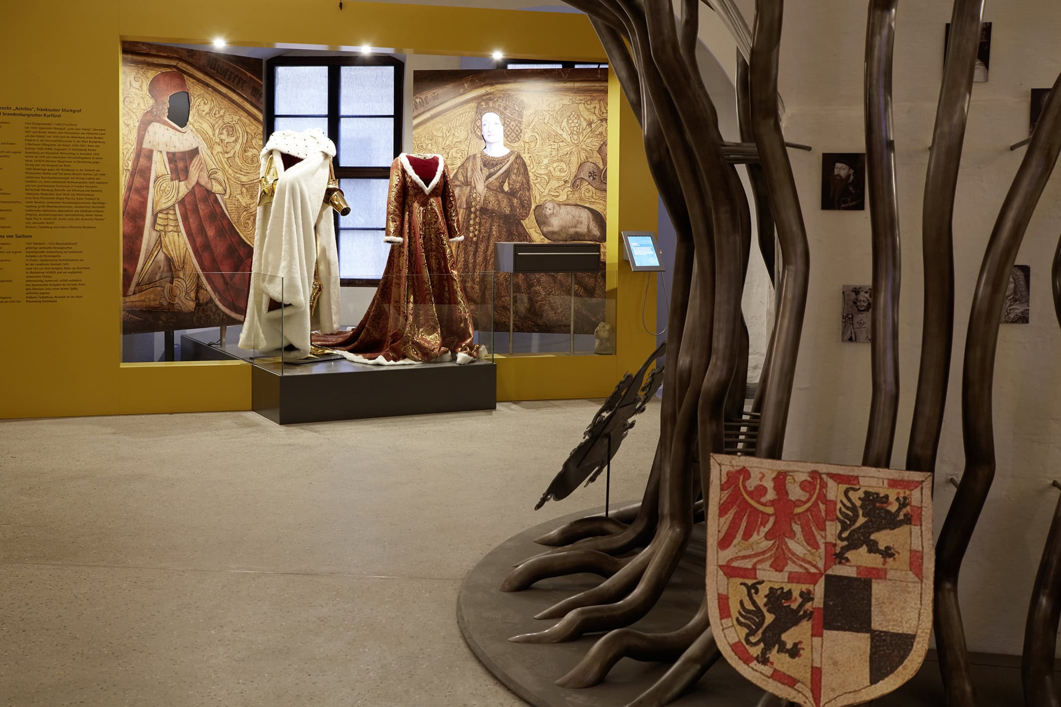 Cadolzburg Castle 3 Museum room with mannequins in Renaissance robes before painted wall murals of Albrecht Achilles and Anna von Sachsen, with metal tree installation displaying heraldic shields