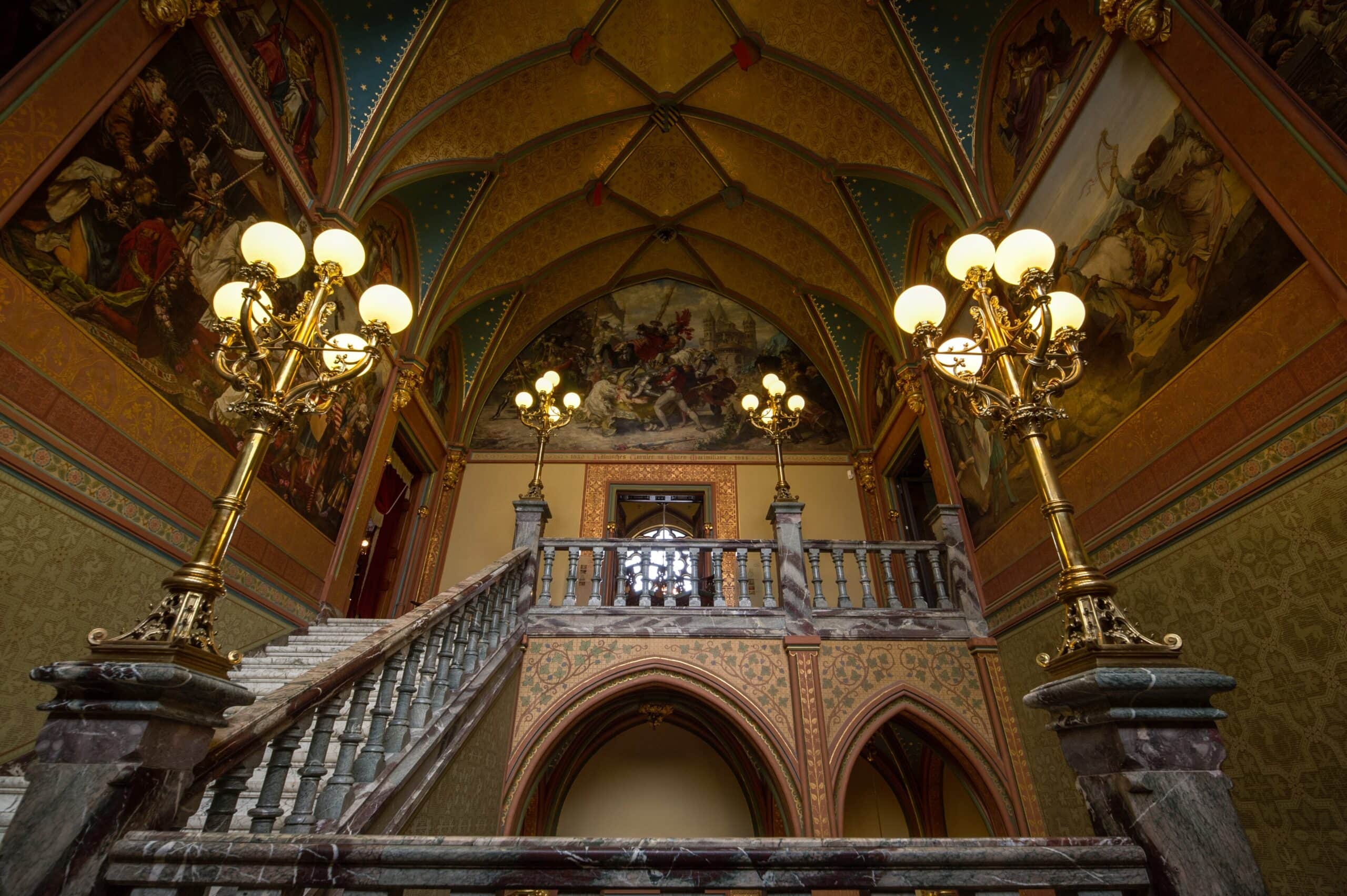 Drachenburg Castle 6 Looking up the grand staircase at Schloss Drachenburg with marble steps, gilded chandeliers and Josef Flüggen's painted Cologne history cycle on the vaulted ceiling above