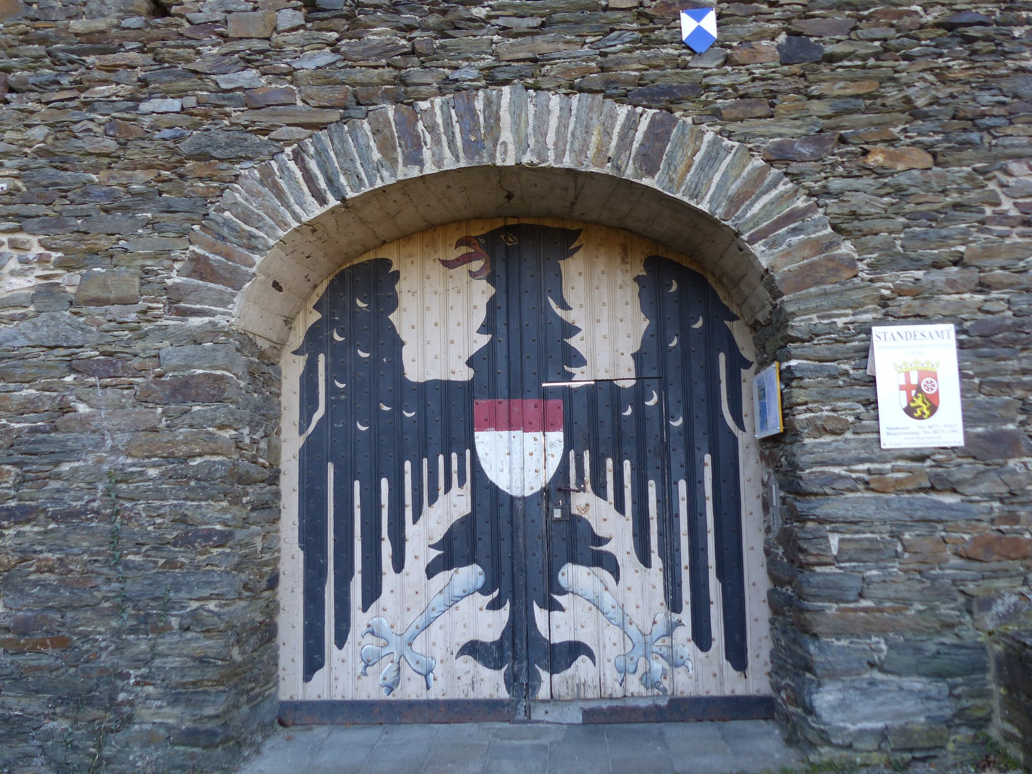 The arched entrance gate of Maus Castle, its timber doors painted with a black imperial eagle bearing the red-and-white Trier shield, a STANDESAMT registry-office sign beside it