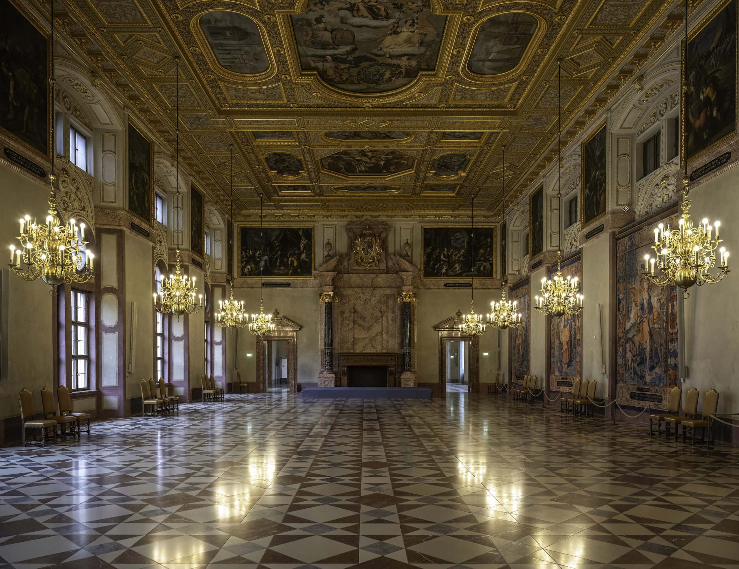 Kaisersaal of Munich Residenz with painted coffered ceiling, chandeliers, fireplace, and tapestries on the walls