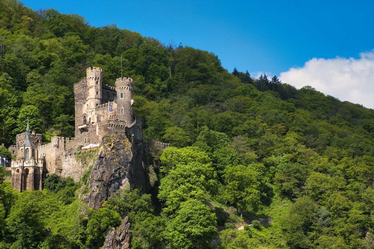 The 19th-Century Romantic Revival of German Castles 4 Burg Rheinstein perched on a slate cliff above the left bank of the Rhine near Trechtingshausen, with the river curving past below.