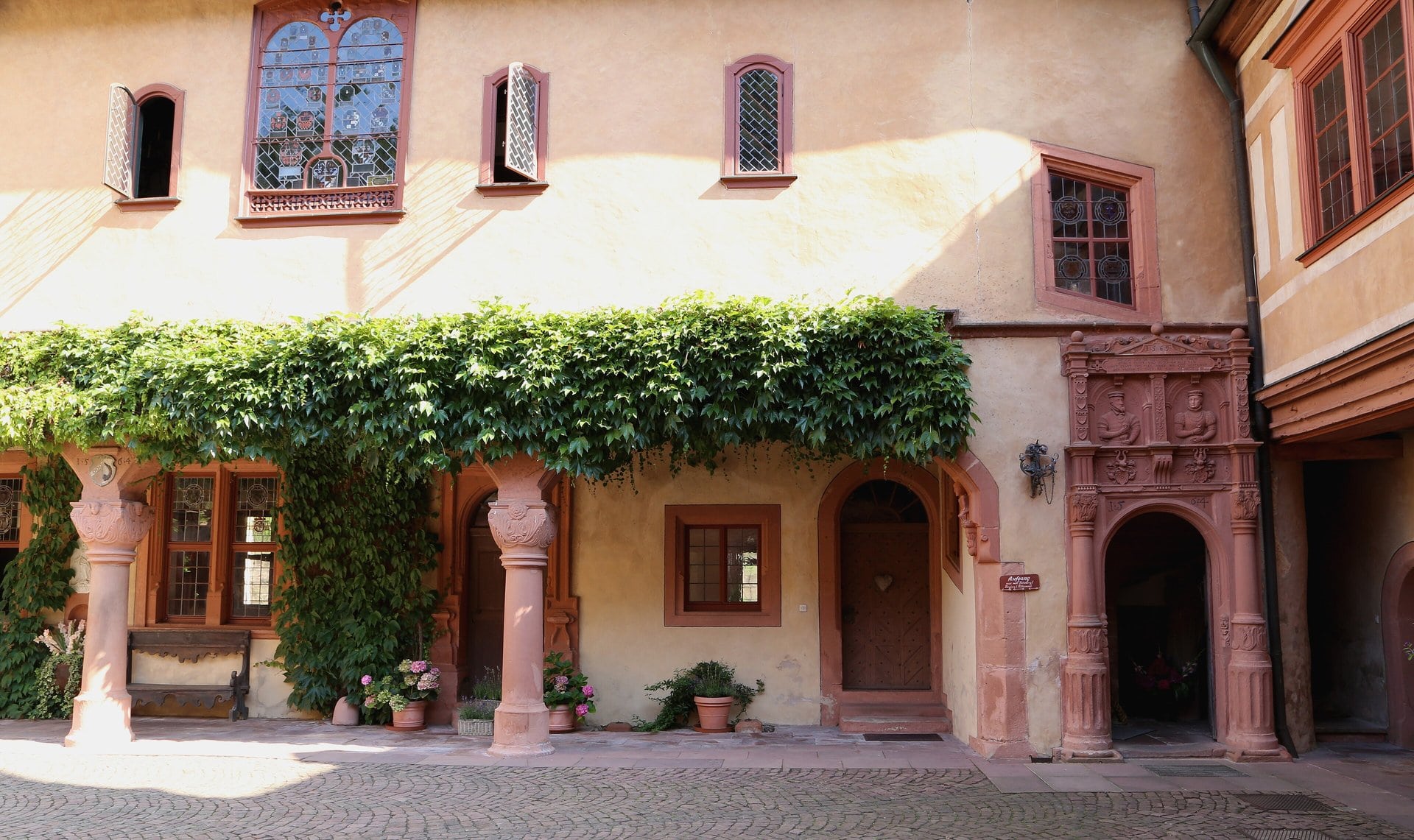 Mespelbrunn Castle 3 The inner courtyard of Schloss Mespelbrunn, showing the 1569 sandstone Renaissance portal of the Treppenturm with carved figures of Peter Echter and Gertraud von Adelsheim above the doorway, an ivy-covered loggia on the left, and the chapel turret rising in the background.