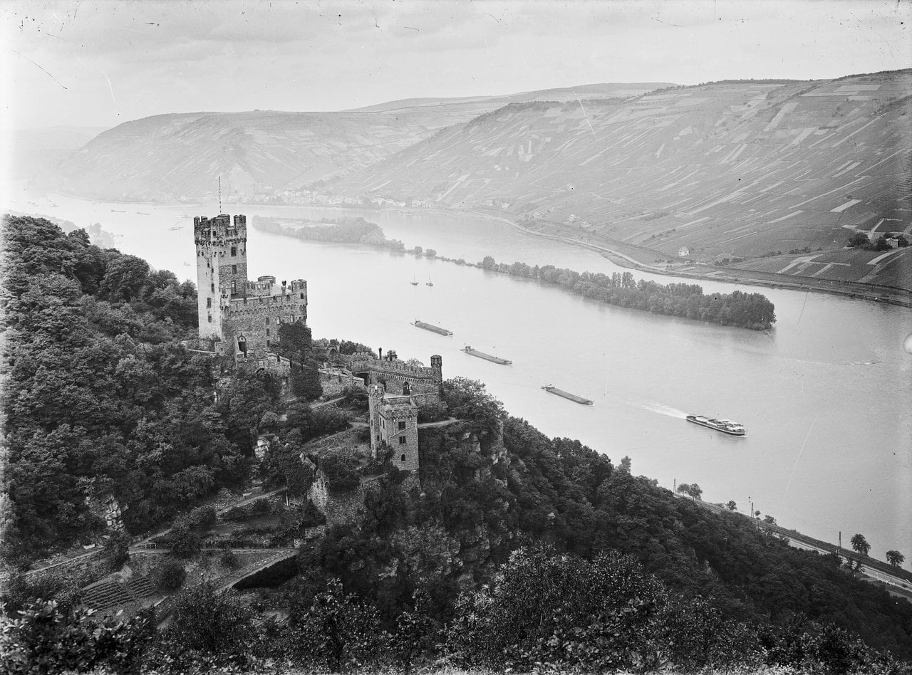Sooneck Castle 2 Black-and-white photograph by Joseph Knippenberg showing Sooneck Castle from above, with cargo barges traveling on the Rhine below.