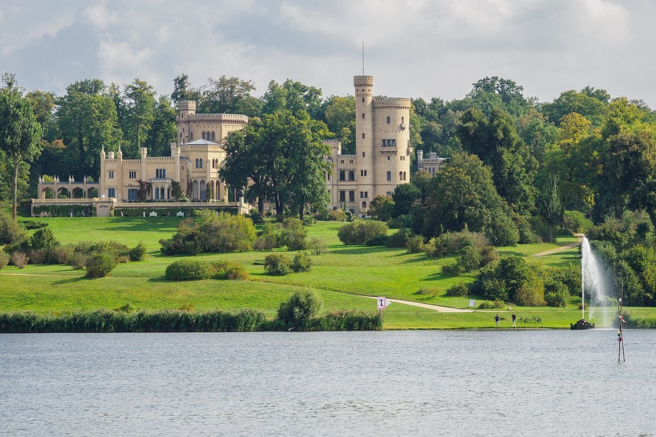 The Garden Palaces of Potsdam 1 Babelsberg Palace seen across the Havel in 2025, crowning the green slope of its landscape park above the river.