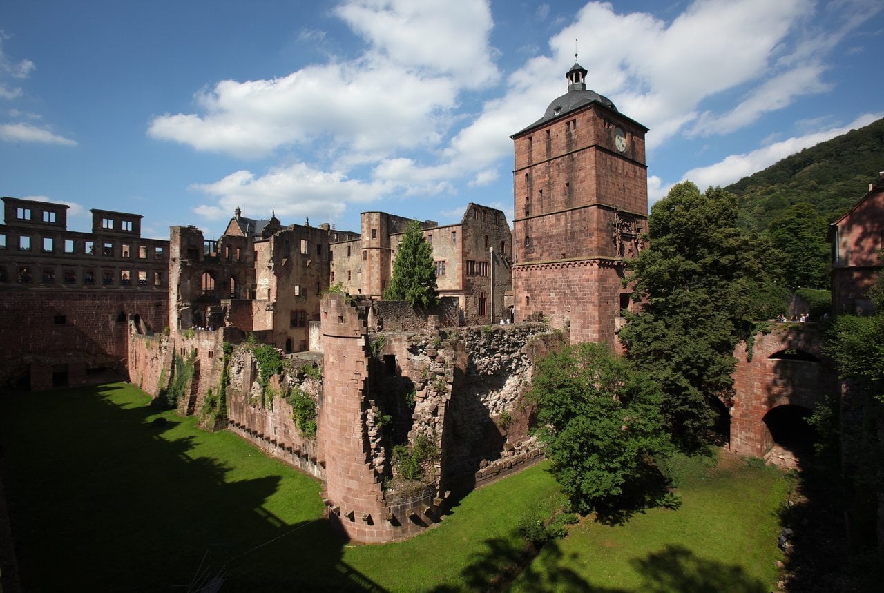 Heidelberg Castle's clock-topped gate tower, ruined wings, and grassy moat seen from outside the walls