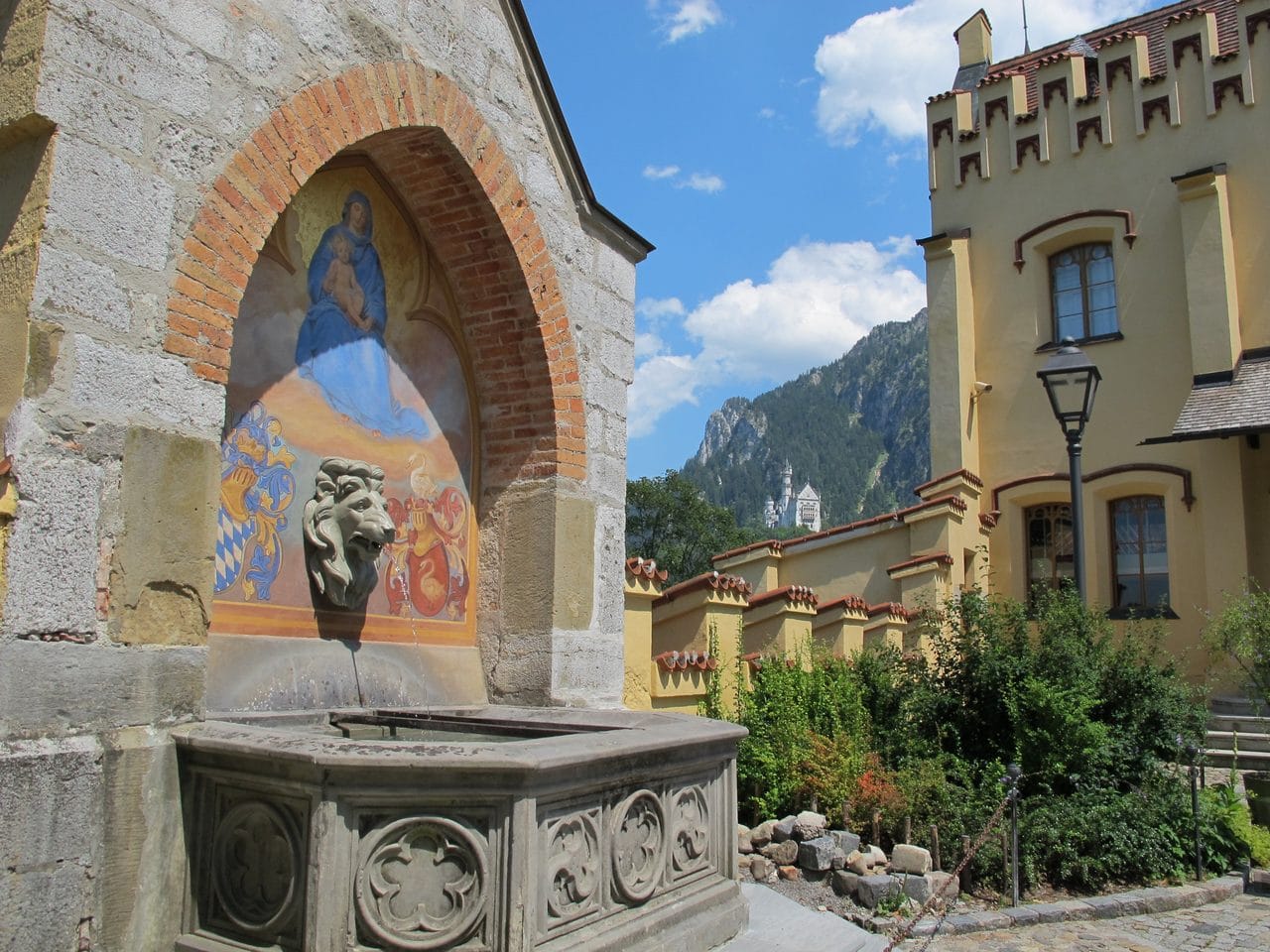 Neuschwanstein seen from Hohenschwangau A wall fountain at Hohenschwangau Castle with Neuschwanstein visible on the ridge beyond