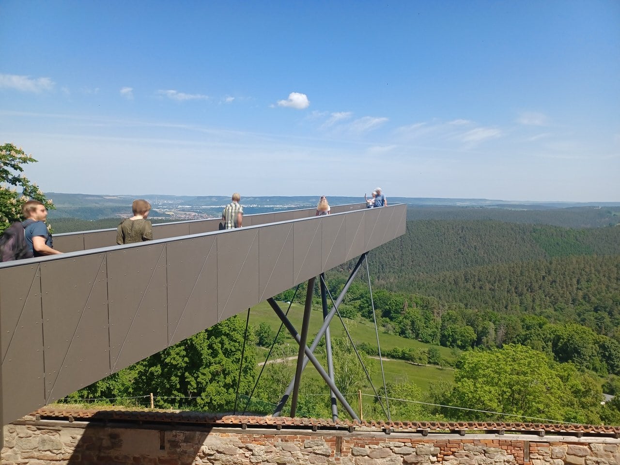 The Steg der Wünsche skywalk — Photo: Enyavar, CC BY-SA 4.0, via Wikimedia Commons Visitors on the cantilevered Steg der Wuensche skywalk projecting from the castle wall over the Saale valley