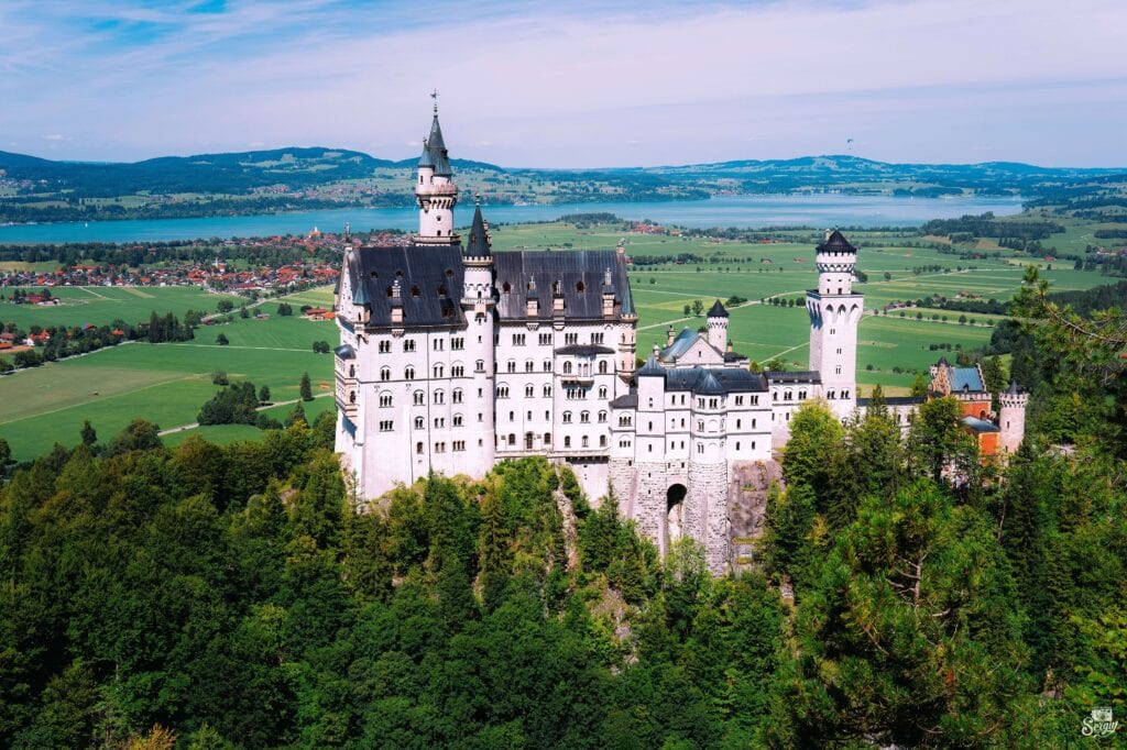 Neuschwanstein Castle 15 An aerial view of Neuschwanstein Castle on its forested ridge, with the Bavarian plain and lakes stretching to the horizon