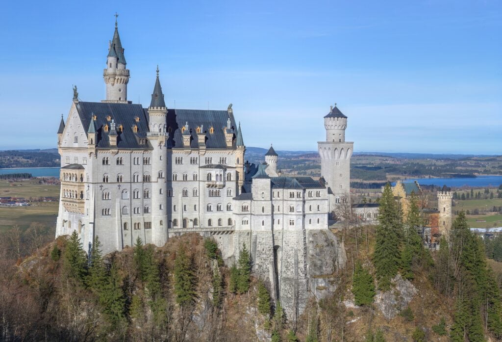 Neuschwanstein Castle 13 Neuschwanstein Castle seen from the southwest, its white limestone walls and towers above forested slopes with the Alpine foothills behind