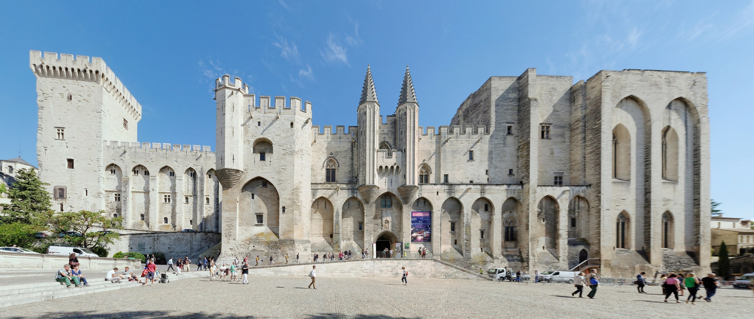 Place du Palais and the Palais des Papes Visitors crossing the Place du Palais before the western facade of the Palais des Papes