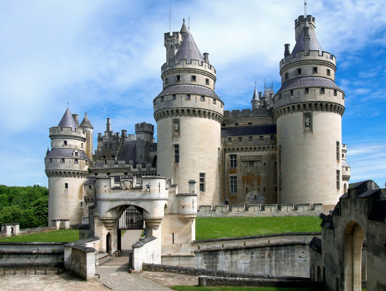 The main entrance today — Rolf Kranz, CC BY-SA 4.0 The twin-towered gatehouse and drawbridge approach of Château de Pierrefonds under a blue sky