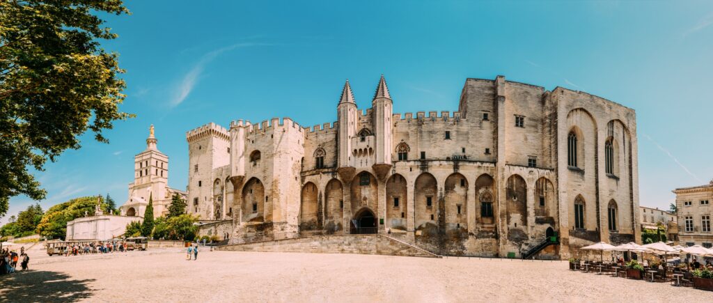 Palais des Papes 14 The full west front of the Palais des Papes seen across the Place du Palais, with the cathedral of Notre-Dame-des-Doms at left