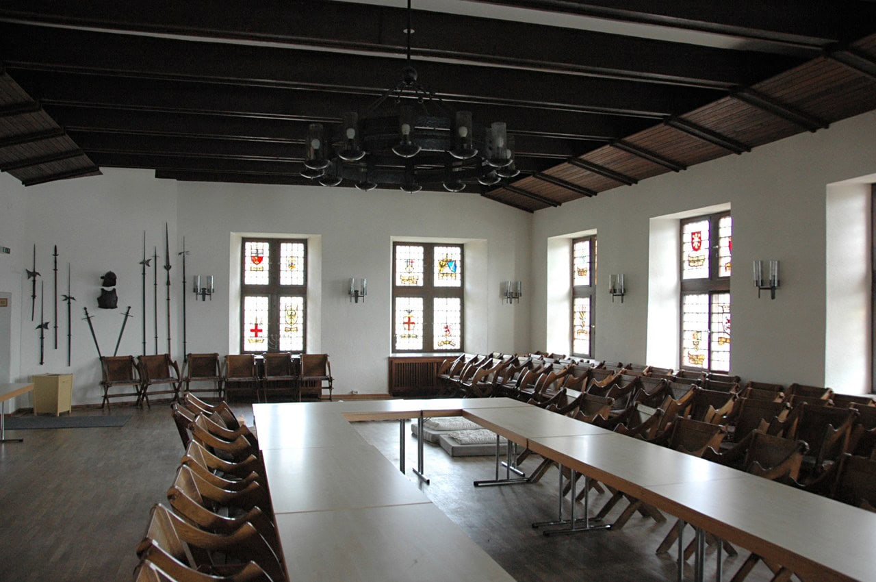 The knights’ hall — Sir Gawain, CC BY-SA 3.0 The Rittersaal of Stahleck Castle with heraldic stained glass.