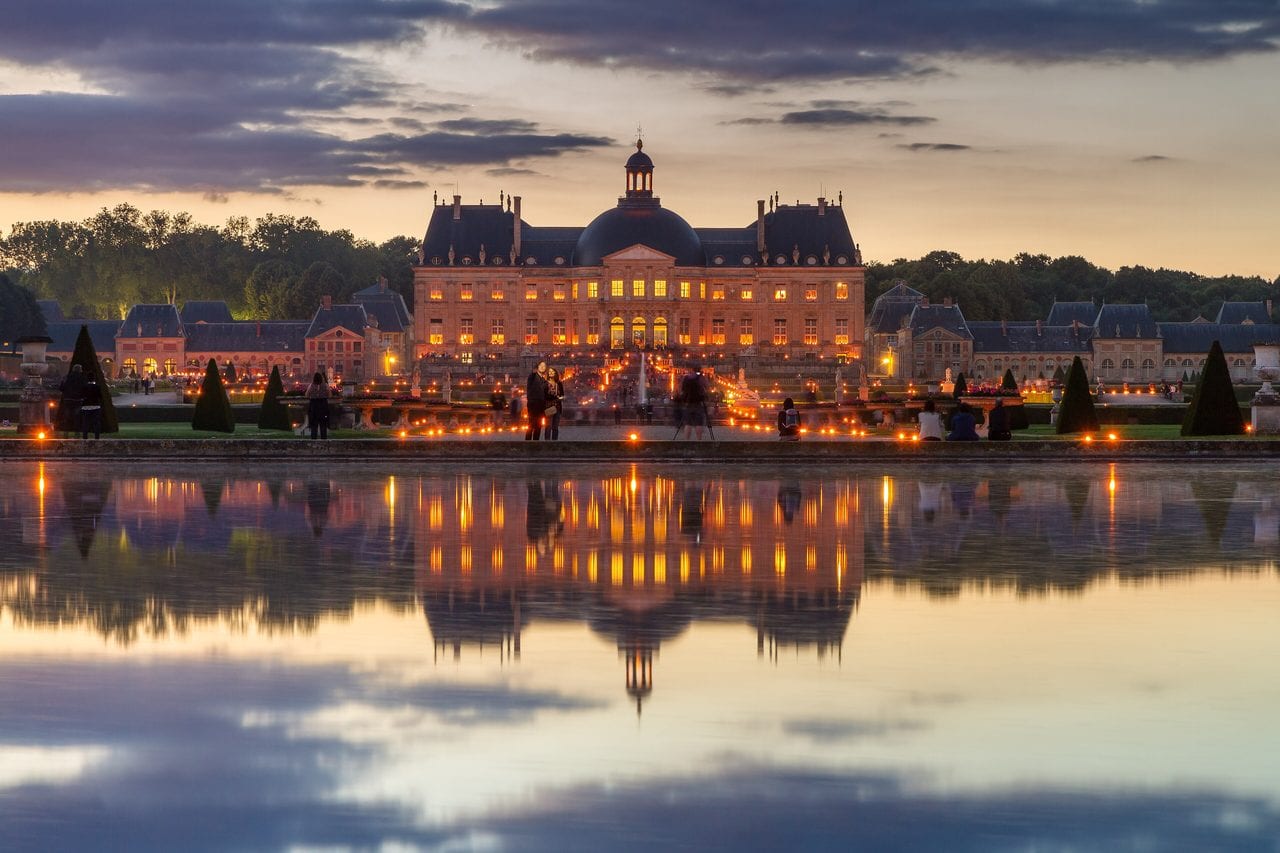 The Chateau de Vaux-le-Vicomte lit by candles at dusk, reflected in the basin