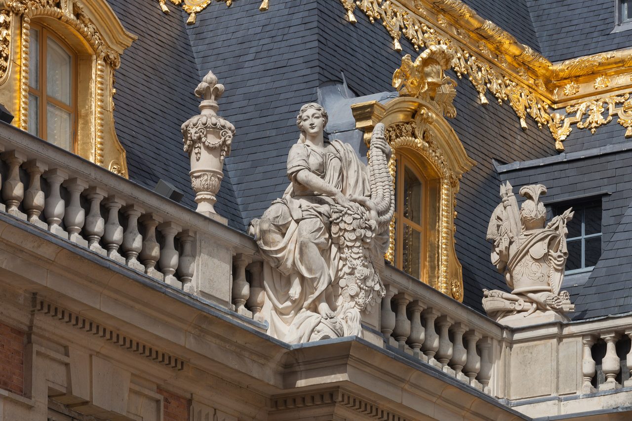 Rooftop statuary — Lmbuga, CC BY-SA 4.0 Gilded rooftop statuary and trophies along the roofline of the Palace of Versailles