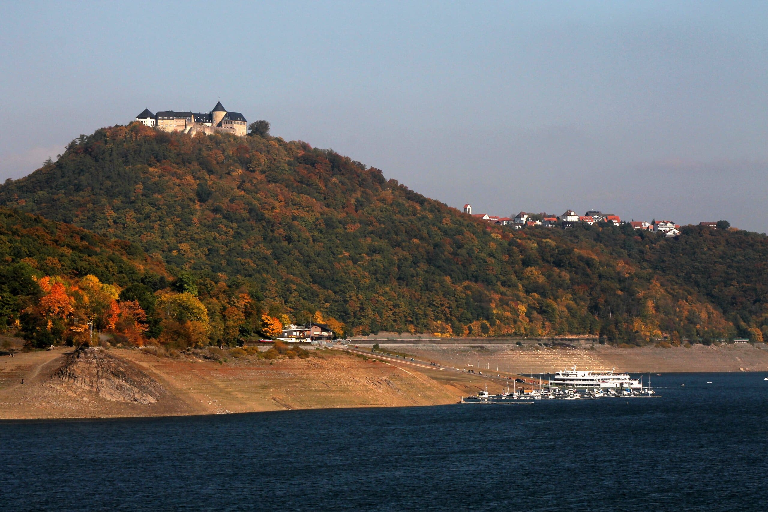 Waldeck Castle above the Edersee at low water in autumn, with the drawn-down shoreline exposed