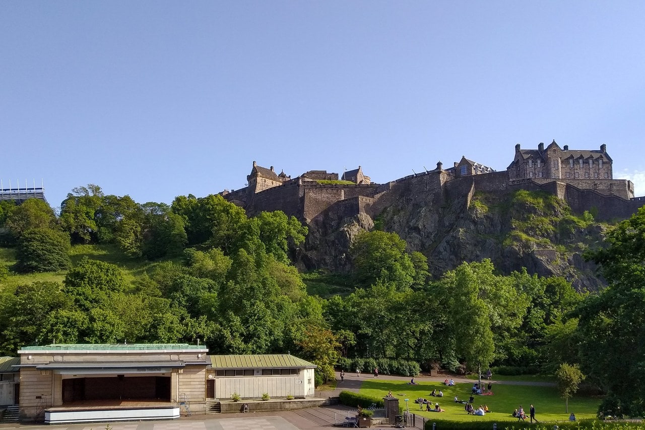 Edinburgh Castle 1 Edinburgh Castle crowns its volcanic crag above the trees of Princes Street Gardens, the ramparts and Royal Palace block clear against a summer sky.