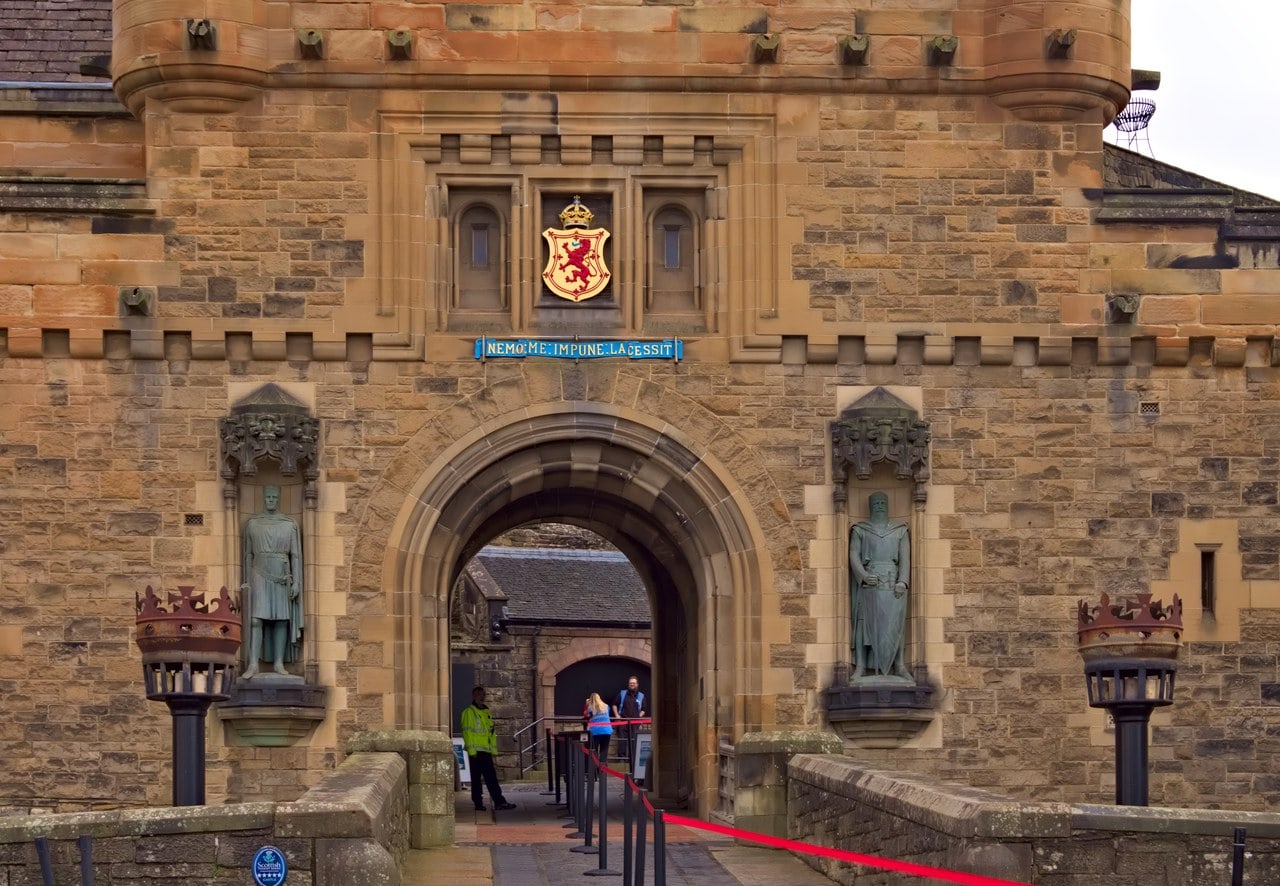The gatehouse entrance of Edinburgh Castle, its arch flanked by bronze statues of Robert the Bruce and William Wallace beneath the royal arms of Scotland and the motto Nemo me impune lacessit. The gatehouse entrance of Edinburgh Castle, its arch flanked by bronze statues of Robert the Bruce and William Wallace beneath the royal arms of Scotland and the motto Nemo me impune lacessit.