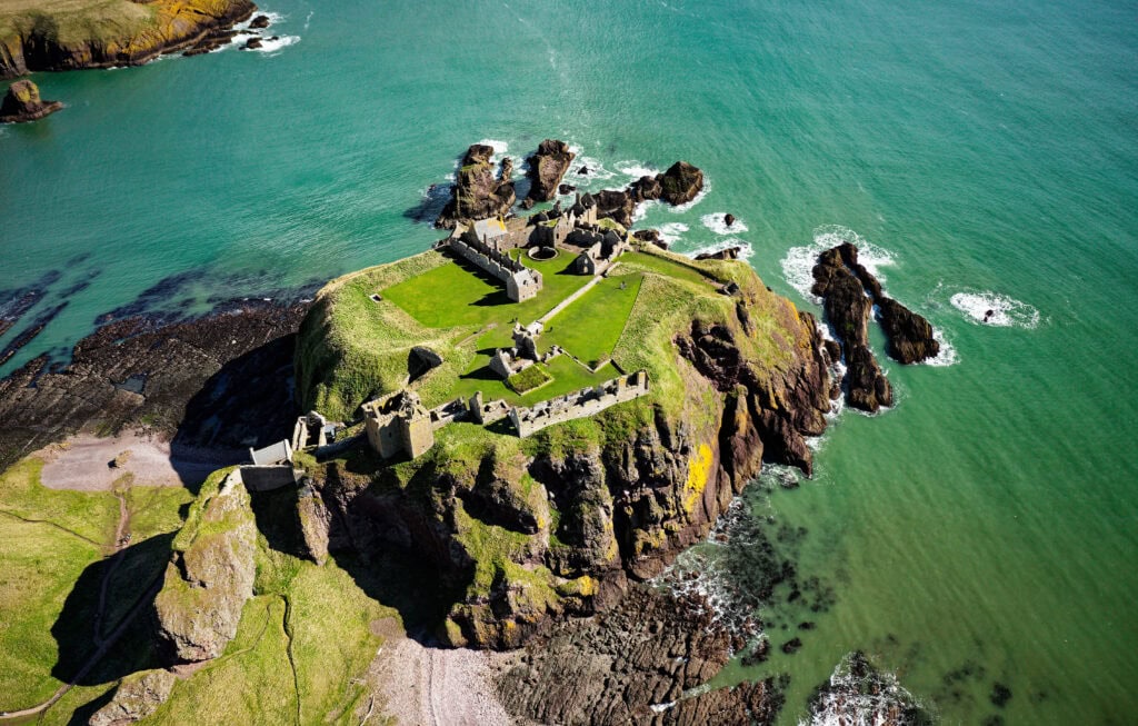 Dunnottar Castle 2 Aerial view of Dunnottar Castle from the seaward side showing the palace ranges at the cliff edge and offshore rock stacks.