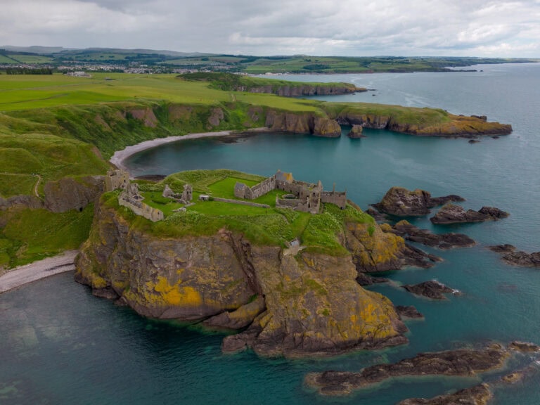 Home 5 Aerial view of Dunnottar Castle on its cliff-top rock with Castle Haven bay and Stonehaven beyond.
