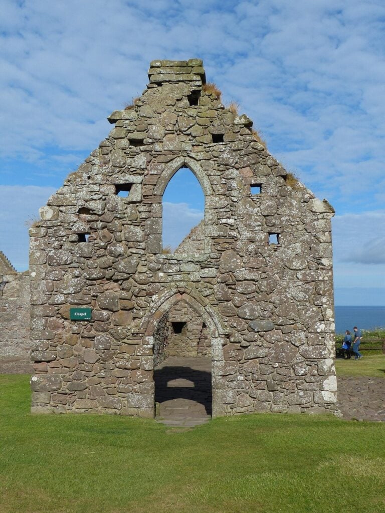 Dunnottar Castle 7 Ruined stone chapel gable at Dunnottar Castle with a tall pointed Gothic window and an arched doorway.