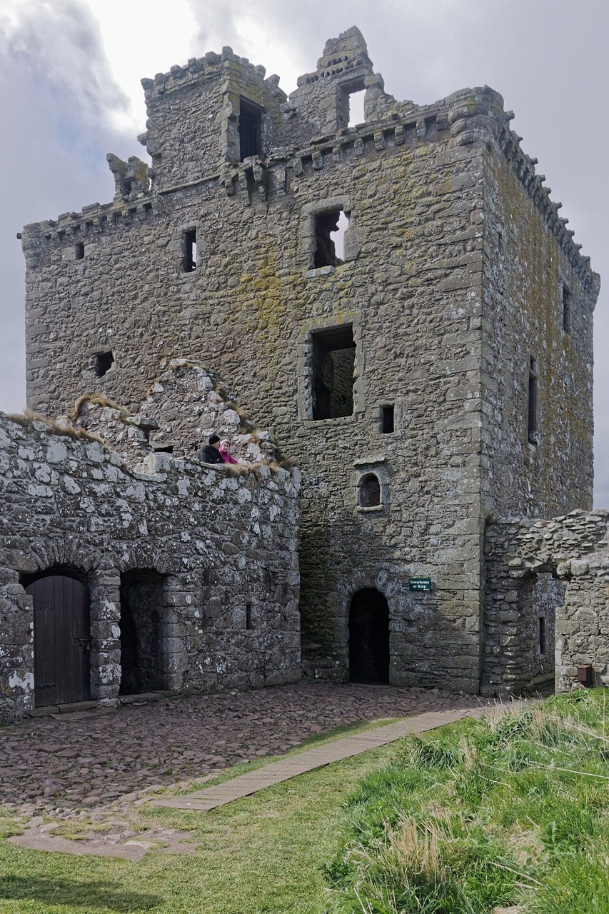 Tall ruined L-plan stone tower house at Dunnottar Castle with a battlemented parapet, seen from the courtyard. Tall ruined L-plan stone tower house at Dunnottar Castle with a battlemented parapet, seen from the courtyard.