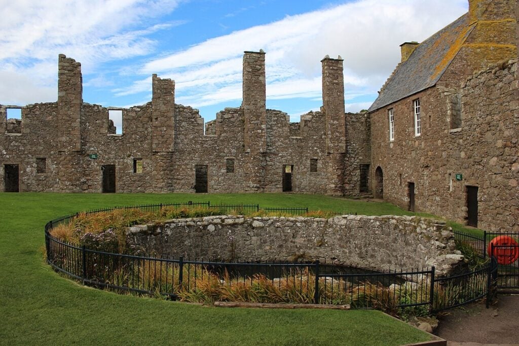 Dunnottar Castle 9 Ruined palace ranges with tall chimney stacks behind a circular walled sunken garden at Dunnottar Castle.