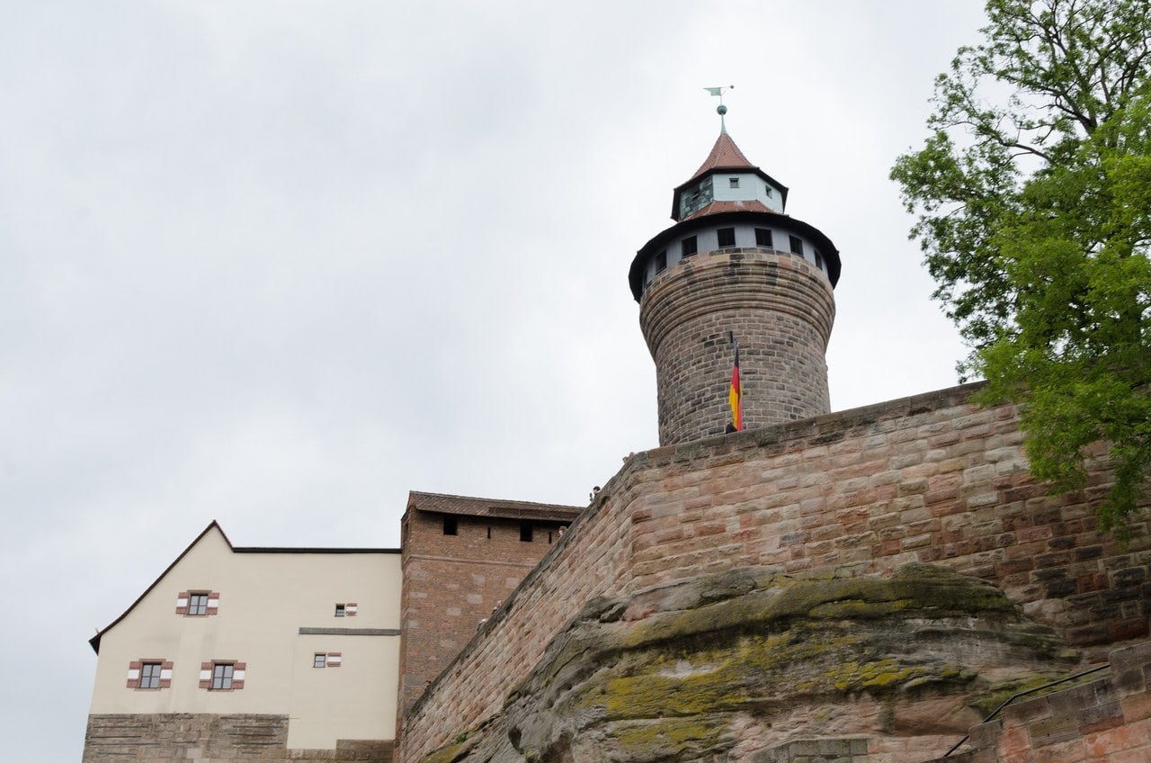 The round Sinwellturm tower of Nuremberg Castle rising above a sandstone outcrop, with a pale residential range standing lower to its left. The round Sinwellturm tower of Nuremberg Castle rising above a sandstone outcrop, with a pale residential range standing lower to its left.