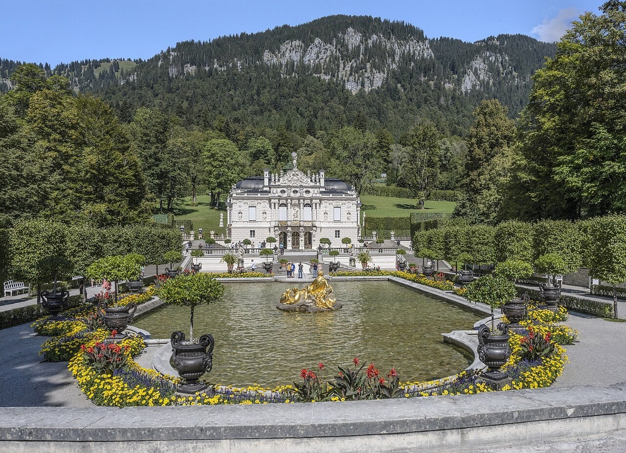 Linderhof Palace above its water parterre and golden fountain, with the forested Ammergau Alps rising behind, Bavaria