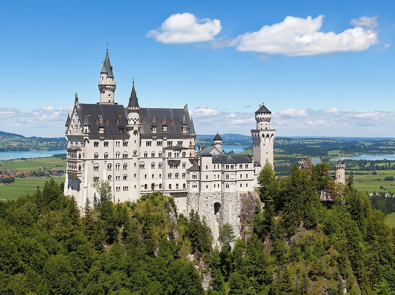 Neuschwanstein Castle on its wooded crag above the Bavarian foothills, with the Forggensee stretching across the plain beyond