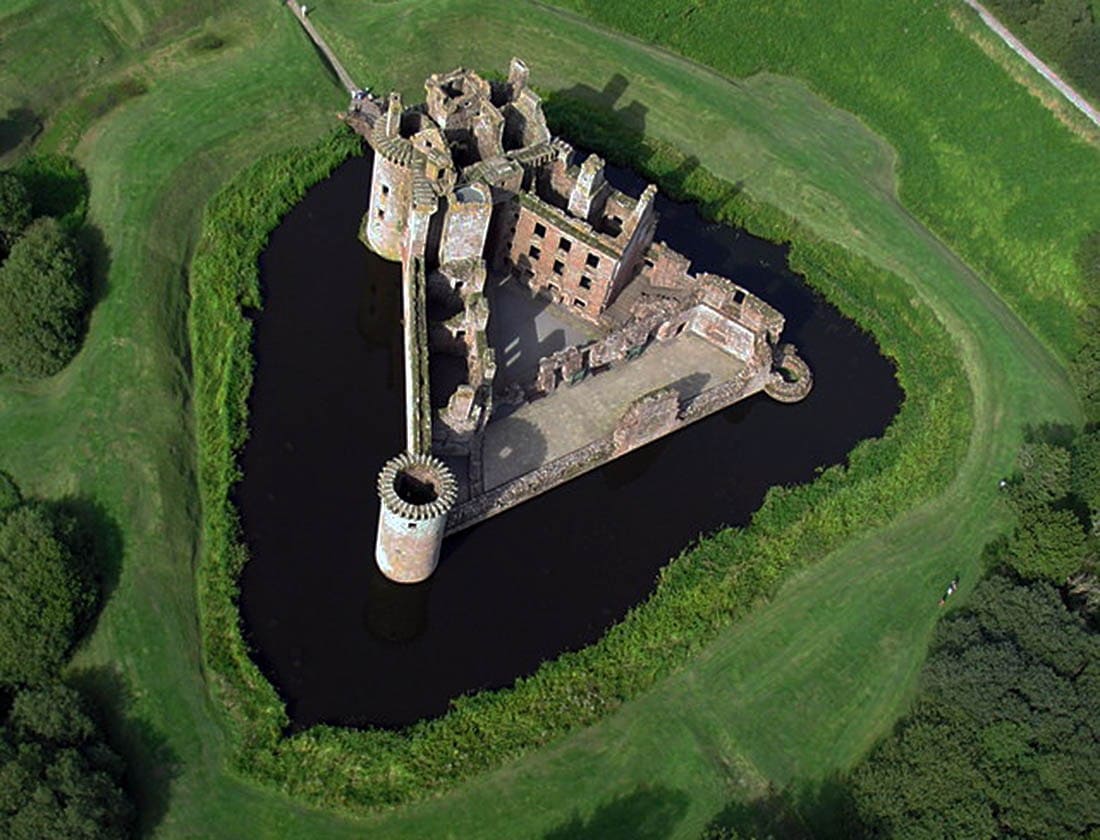 Aerial view of the triangular Caerlaverock Castle enclosed by a water-filled moat, with a bridge crossing to the twin-towered gatehouse Aerial view of the triangular Caerlaverock Castle enclosed by a water-filled moat, with a bridge crossing to the twin-towered gatehouse