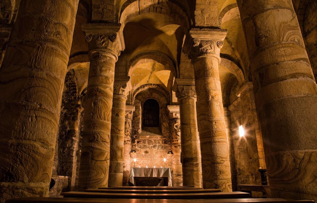 Interior of the Norman Chapel at Durham Castle, with squat stone columns, carved capitals, groin vaults and a small altar lit by candles. Interior of the Norman Chapel at Durham Castle, with squat stone columns, carved capitals, groin vaults and a small altar lit by candles.