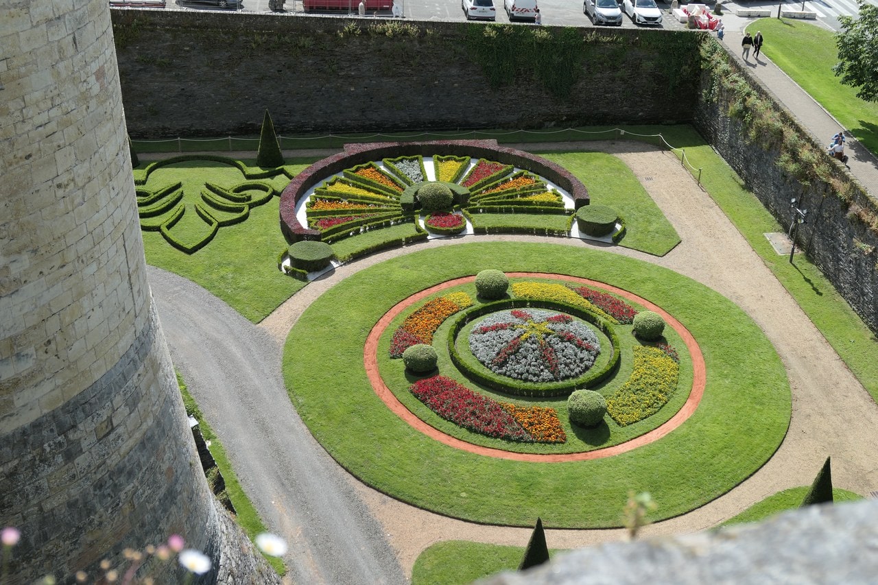 Formal parterre gardens laid out on the floor of the dry ditch at Chateau d'Angers, seen from the rampart walk beside a banded drum tower Formal parterre gardens laid out on the floor of the dry ditch at Chateau d'Angers, seen from the rampart walk beside a banded drum tower