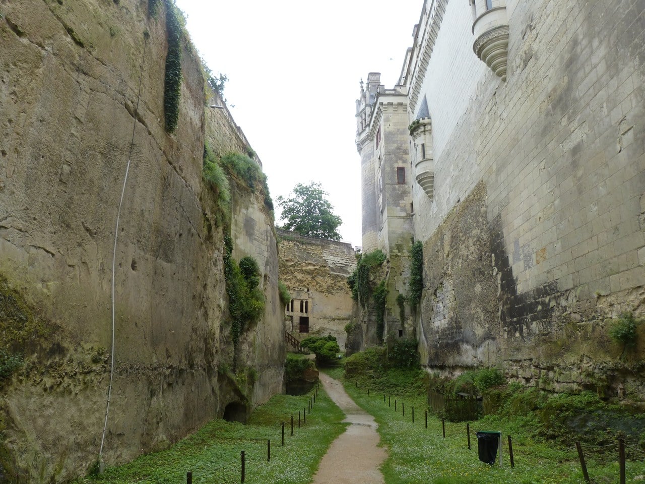 Looking along the floor of the deep dry moat at Chateau de Breze, rock-cut walls rising on both sides with the chateau far above Looking along the floor of the deep dry moat at Chateau de Breze, rock-cut walls rising on both sides with the chateau far above