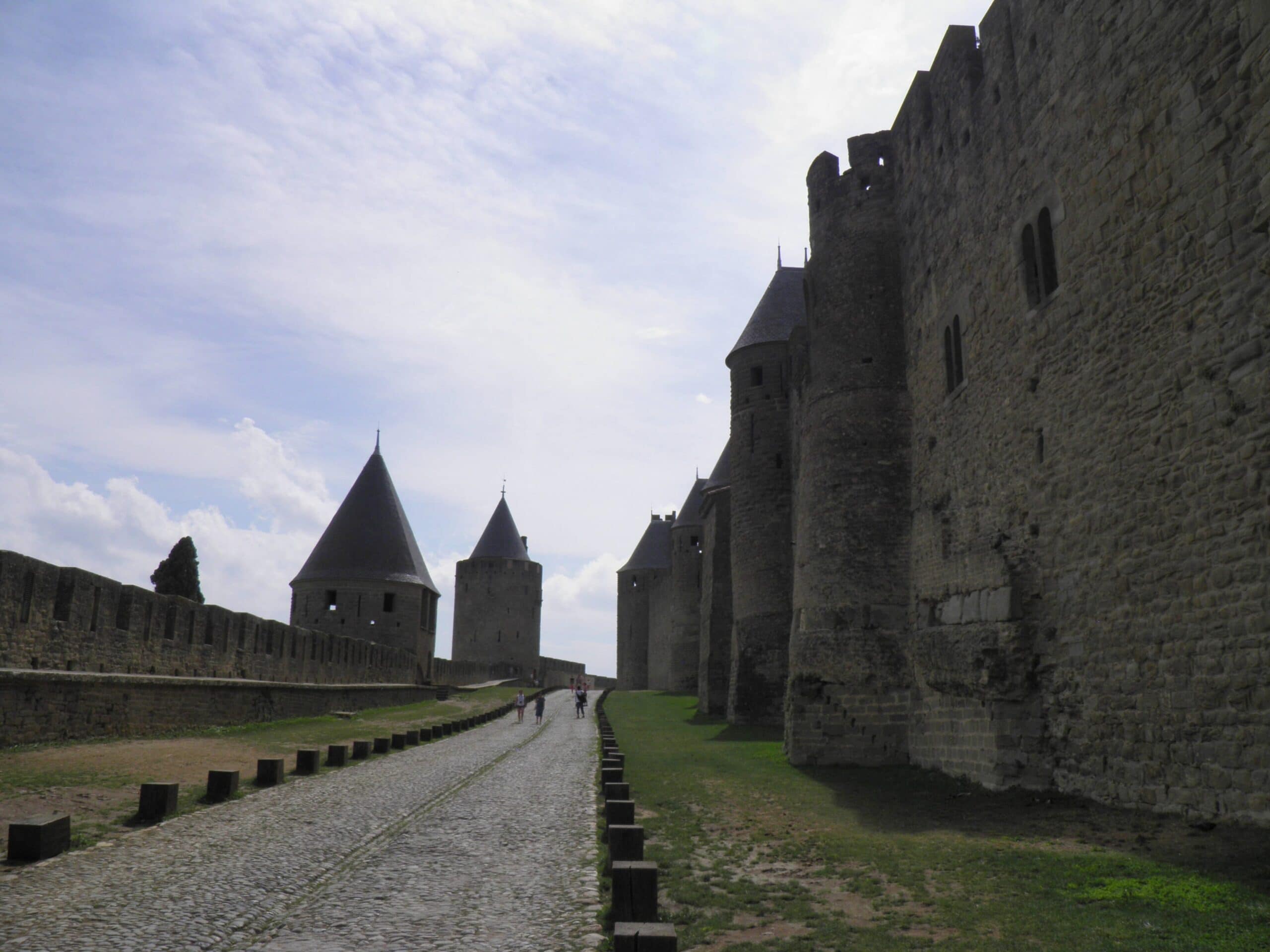 Two parallel defensive walls at Carcassonne with a grassy, cobbled corridor, the lices, running between the tall inner curtain and its towers and the lower crenellated outer wall. Carcassonne's two parallel defensive walls with the grassy lices corridor between the inner curtain and outer wall.