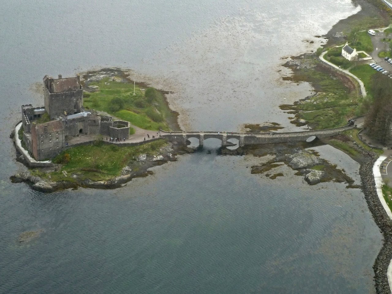 An elevated view shows the whole island, the castle and its footbridge reaching across the tidal narrows to the mainland shore. An elevated view shows the whole island, the castle and its footbridge reaching across the tidal narrows to the mainland shore.