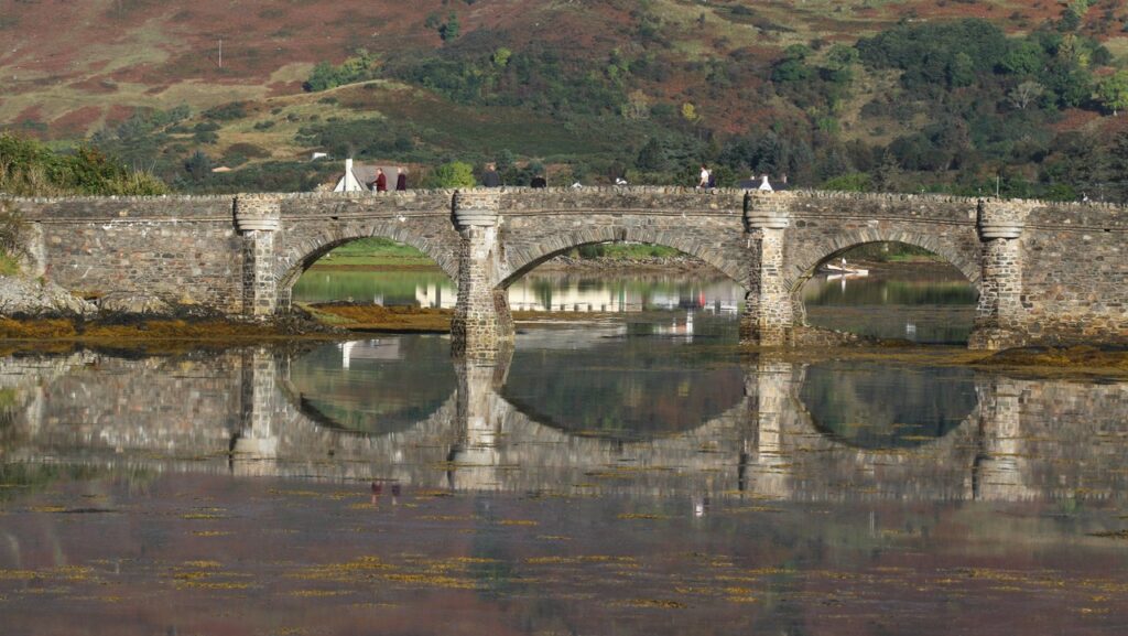 Eilean Donan Castle 5 Three low arches of the castle's footbridge and their reflections span the shallow water at the island's edge.