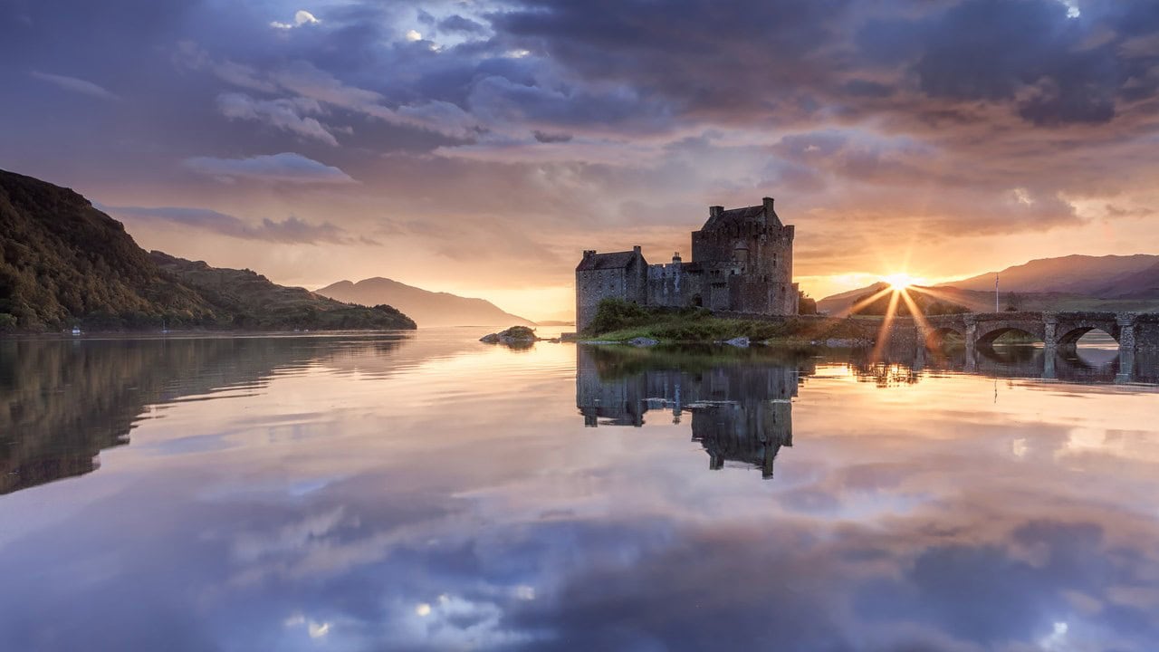 The castle and its footbridge silhouetted at sunset, the burning sky mirrored in the calm loch. The castle and its footbridge silhouetted at sunset, the burning sky mirrored in the calm loch.