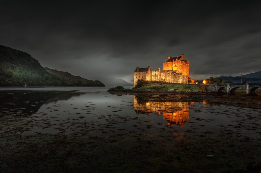 Eilean Donan Castle 9 Floodlit against a near-black storm sky, Eilean Donan mirrors in the tidal shallows of Loch Duich at blue hour.
