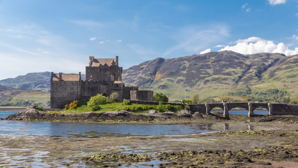Eilean Donan Castle 6 The castle and its bridge on a bright day, backed by the hills above Loch Duich at low tide.