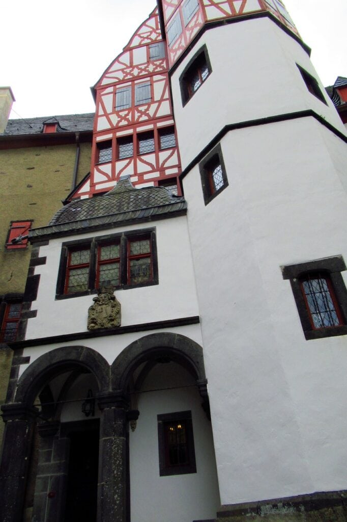 A named-house facade at Burg Eltz with a stone loggia, carved arms, octagonal stair tower and half-timbered gable