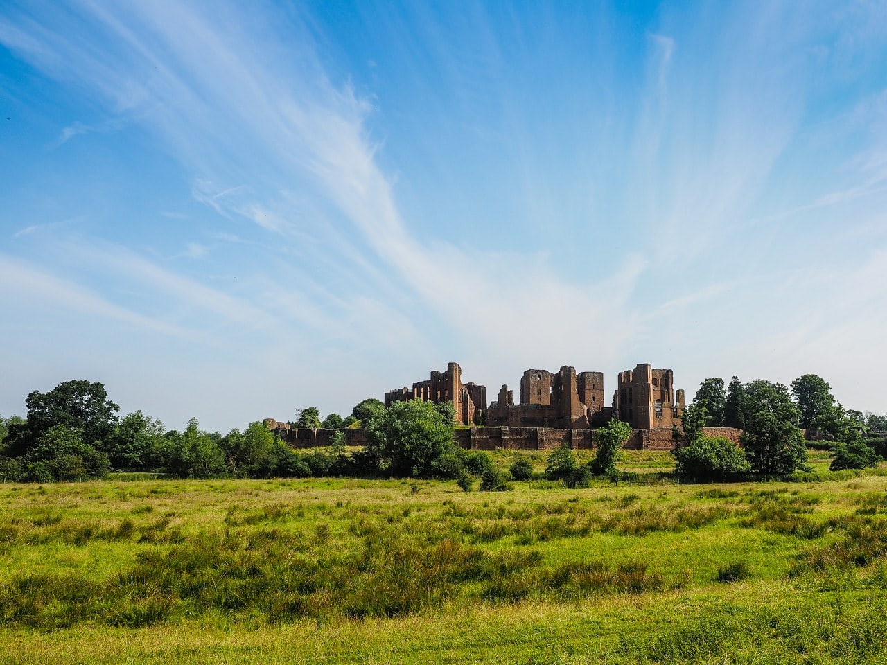 The ruins of Kenilworth Castle seen from the south across a wide, flat meadow of rough grass The ruins of Kenilworth Castle seen from the south across a wide, flat meadow of rough grass