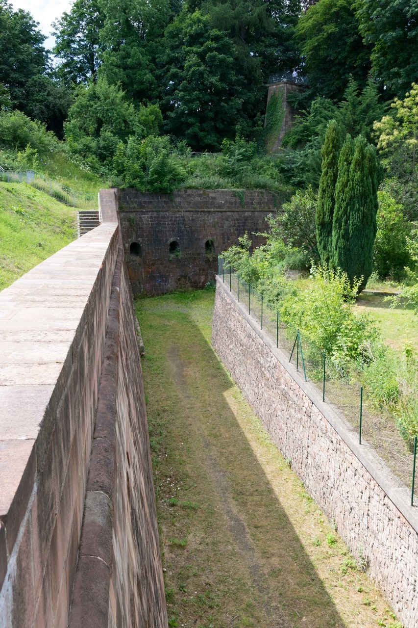A dry neck ditch at Marburg Castle running away between two revetted stone walls, with three round openings pierced low in the masonry ahead A dry neck ditch at Marburg Castle running away between two revetted stone walls, with three round openings pierced low in the masonry ahead