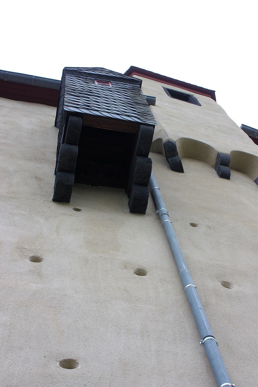 Looking steeply up a rendered wall at Marksburg to a small timber box with a slate roof, carried on stone corbels and open underneath, with a blank wall below it. Looking steeply up a rendered wall at Marksburg to a small timber box with a slate roof, carried on stone corbels and open underneath, with a blank wall below it.