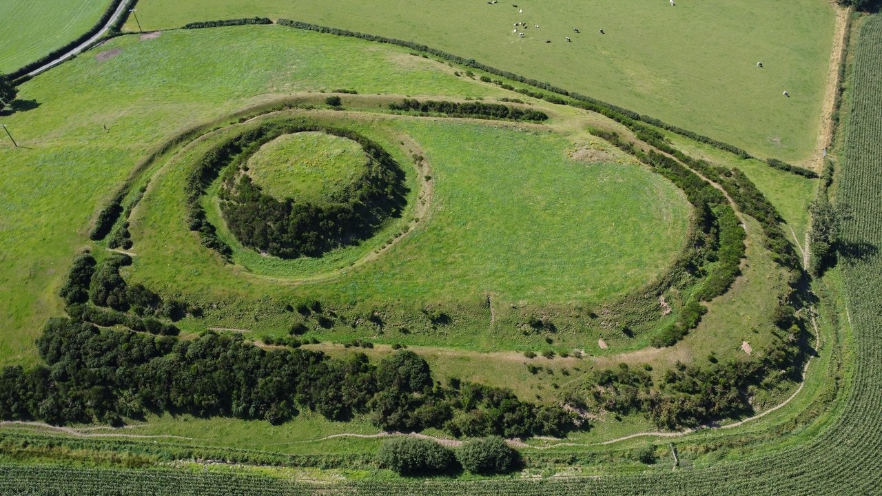 Aerial view of the Motte of Urr in Scotland, a flat-topped grassy mound ringed by a ditch and set inside a large oval bailey with a bank. Aerial view of the Motte of Urr in Scotland, a flat-topped grassy mound ringed by a ditch and set inside a large oval bailey with a bank.